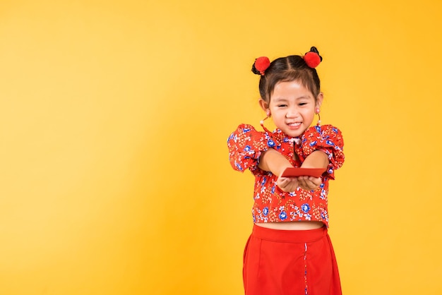 Sonrisa de niña china asiática feliz usar cheongsam rojo entregado angpao o regalo monetario de paquete rojo