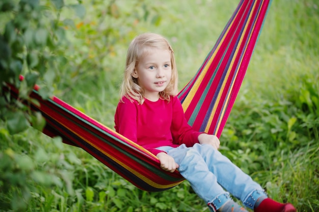 Sonrisa a niña rubia en hamaca en el jardín