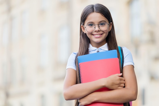 Sonrisa de niño pequeño feliz en anteojos sosteniendo libros escolares al aire libre espacio de copia de conocimiento