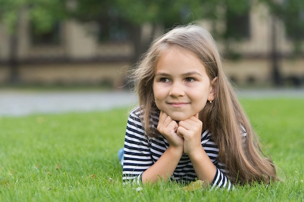 Sonrisa de niño pequeño feliz con piel de cara sana y cabello largo acostado sobre hierba verde cuidado de la piel de paisaje de verano natural