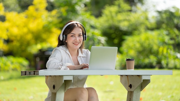 Sonrisa pensativa Mujer feliz haciendo videollamadas en línea o reuniéndose en línea trabajando con una computadora portátil en un parque