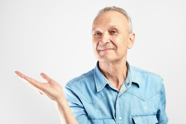 Sonrisa positiva de abuelo canoso fingiendo estar sosteniendo algo en la palma de la mano en un estudio blanco aislado con espacio para copiar