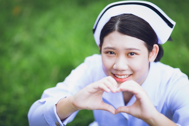 Sonrisa de primer plano uniforme de enfermera asiática tailandesa linda con forma de corazón de mano para compartir amor y concepto de salud de personas de cuidado.