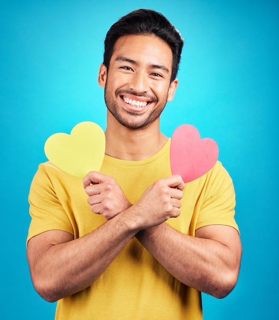 Sonrisa de retrato y hombre con corte de corazón en estudio aislado en un fondo azul Felicidad de amor y persona asiática con signo de símbolo o emoji para cuidado de afecto y empatía romántica y San Valentín