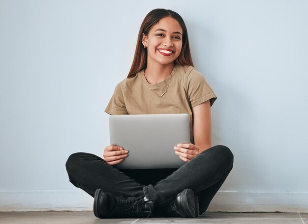 Foto sonrisa de retrato y mujer estudiante con computadora portátil en casa para estudiar aprendizaje o educación computadora de tecnología y mujer feliz sentada en el piso con pc para investigar sobre el fondo de la pared para maqueta