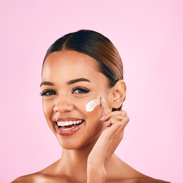 Sonrisa de retrato de mujer feliz y crema para el cuidado de la piel para humectante de belleza contra un fondo de estudio rosa Mujer o modelo sonriendo de felicidad por productos cosméticos de loción o tratamiento facial