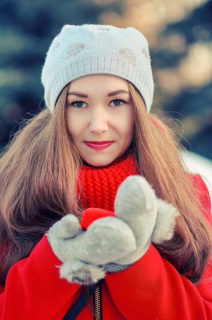 Sonrisa de Yong chica con cabello largo en un abrigo rojo y bufanda con el regalo en una caja roja. Retrato de invierno al aire libre.