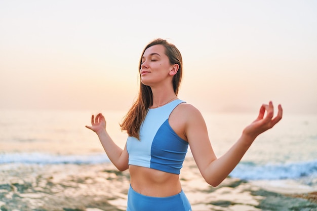 Sonzentrierte, glückselige Fitnessfrau mit geschlossenen Augen, die allein mit Händen in Meditationsposition steht, während sie atmet, Psychische Pflege und gesunde Gewohnheiten