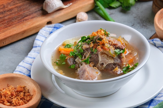 Sop Buntut oder Ochsenschwanzsuppe wird in einer weißen Schüssel auf rustikalem grauem Hintergrund serviert. indonesische traditionelle Küche