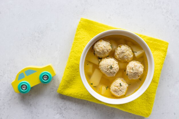 Sopa de albóndigas para niños con picatostes con coche de juguete y mantel amarillo