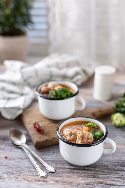 Sopa con albóndigas en tazas de metal sobre mesa de madera