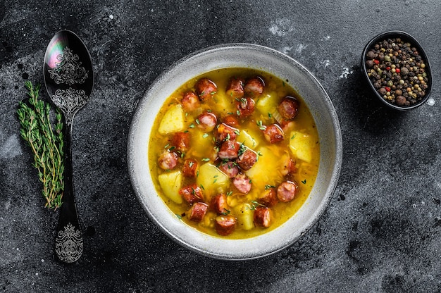 Sopa alemã de ervilha com linguiça defumada e carne. Fundo preto. Vista do topo.