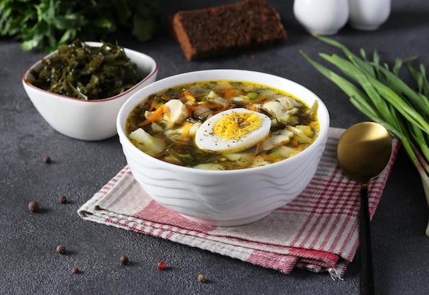 Sopa de algas y pollo servida con huevo hervido en un tazón blanco sobre fondo gris oscuro