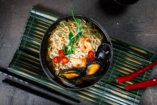 Sopa asiática com macarrão ramen, com pasta de missô, molho de soja, mexilhões e camarão. Em uma mesa de pedra escura, com pauzinhos. Copiar espaço