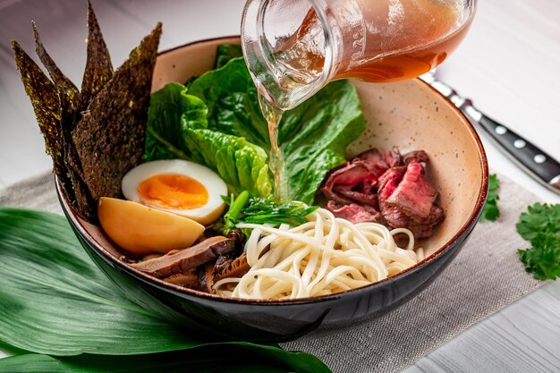Sopa asiática de ramen con fideos de arroz, champiñones y carne de cerdo en un tazón negro Cocina asiática