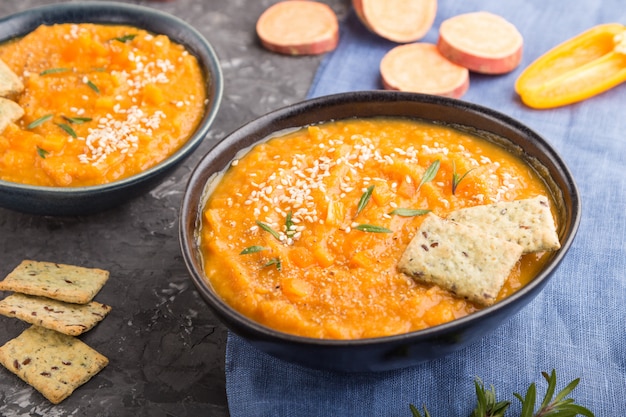 Sopa de batata o crema de batata con semillas de sésamo y aperitivos en cuencos de cerámica azul sobre una superficie de hormigón negro. vista lateral, enfoque selectivo