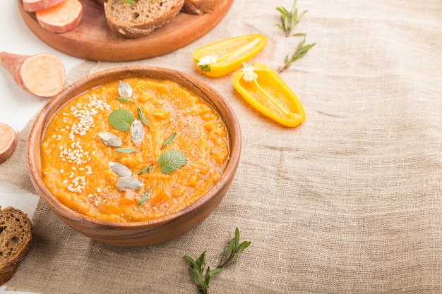 Sopa de batata o crema de batata con semillas de sésamo en un recipiente de madera sobre un fondo blanco de madera. Vista lateral, enfoque selectivo, copia espacio.