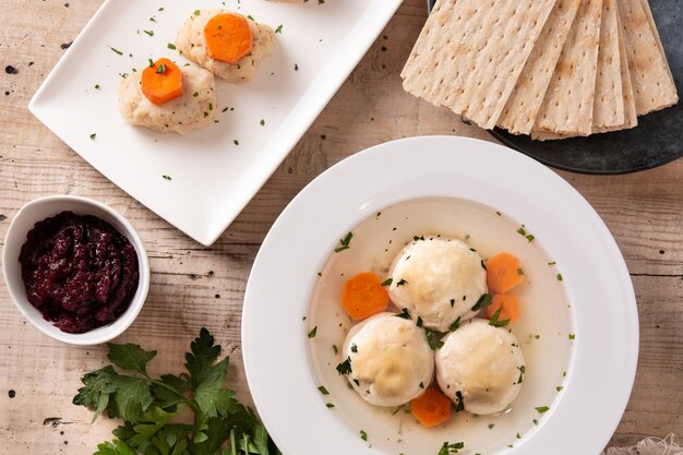 Sopa bola de matzá judaica tradicional, gefilte fish e pão matzá na mesa de madeira