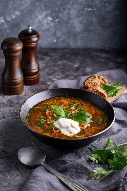 Sopa borsch tradicional europea y rusa con col, crema agria y carne servida en un plato sobre una mesa de piedra oscura