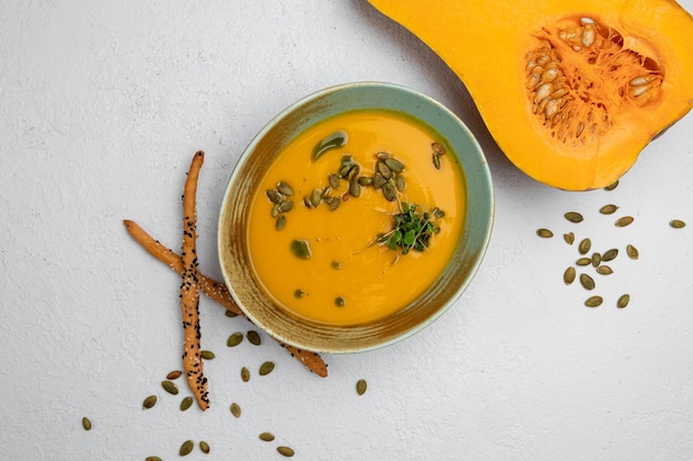 Sopa de calabaza adornada con semillas de calabaza sobre un fondo blanco.