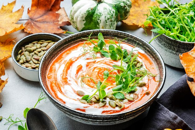 Sopa de calabaza con crema de semillas y brotes de guisantes verdes Comida lenta saludable de invierno u otoño Tazón de sopa sobre fondo de mesa gris Vista superior