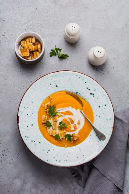 Sopa de calabaza con crema, trozos de pan y nueces de cedro en placa de cerámica gris sobre fondo gris de mesa. Comida tradicional de otoño. Espacio de copia de vista superior.