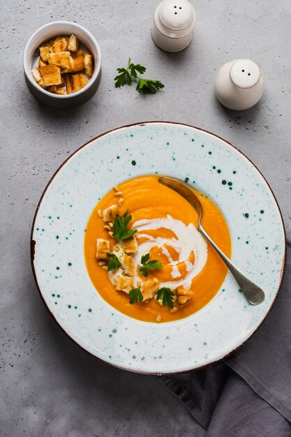 Sopa de calabaza con crema, trozos de pan y nueces de cedro en placa de cerámica gris sobre la superficie de la mesa gris