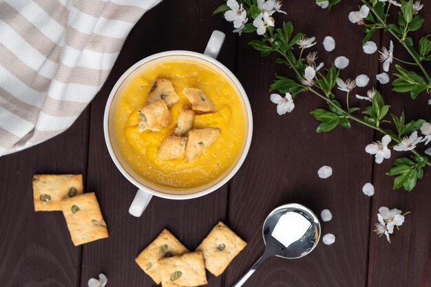 Sopa de calabaza cremosa orgánica picante fresca en un tazón blanco sobre una mesa de madera con galletas de pan