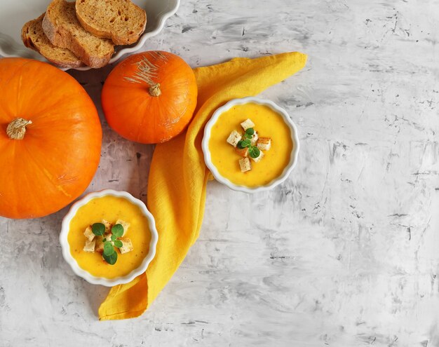 Sopa de calabaza en dos tazones con rebanadas de pan y calabazas, vista superior