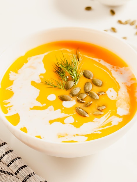 Sopa de calabaza en una mesa blanca con servilleta de semillas de calabaza pov