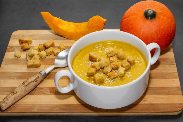 Sopa de calabaza de otoño con semillas de sésamo sobre un fondo de madera. Sopa en un plato y rodajas de calabaza sobre un fondo de madera