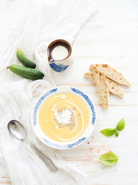 Sopa de calabaza con pepinos de albahaca fresca crema y pan en plato de cerámica vintage sobre fondo de madera blanca vista superior