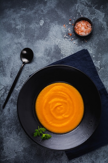 Sopa de calabaza en placa de cerámica negra sobre fondo de madera oscura. comida tradicional de otoño. espacio de copia de vista superior.