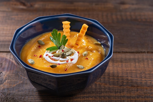 Sopa de calabaza en plato azul sobre mesa de madera decorada con semillas de calabaza y concepto de recetas de temporada de otoño de perejil