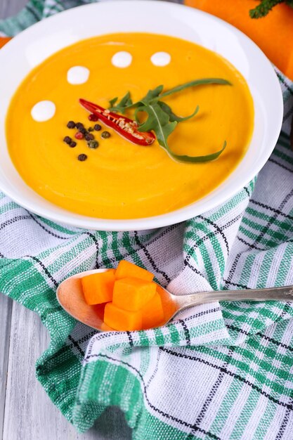 Sopa de calabaza en plato blanco y rodaja de calabaza en servilleta sobre fondo de madera