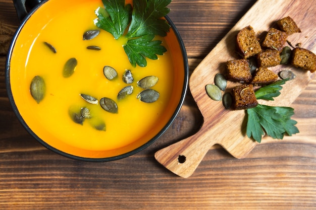 Sopa de calabaza en un recipiente con semillas y perejil sobre un fondo de madera. Galletas con especias en el tablero. Copie el espacio. Acción de gracias, sopa de otoño