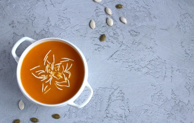 Sopa de calabaza con salsa y semillas de calabaza en una taza blanca sobre un fondo gris