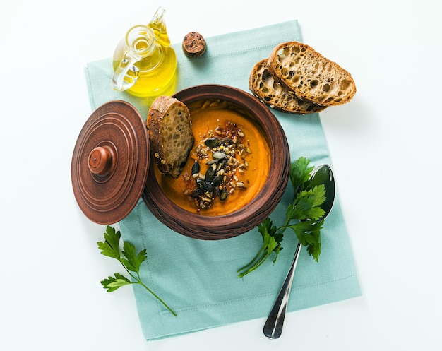 Sopa de calabaza con semillas y pan de centeno fresco en un recipiente de arcilla sobre una mesa