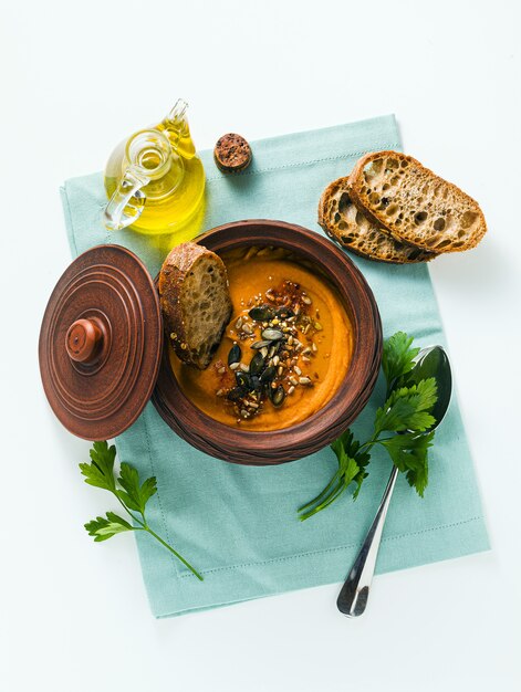 Sopa de calabaza con semillas y pan de centeno fresco en un recipiente de arcilla sobre la mesa