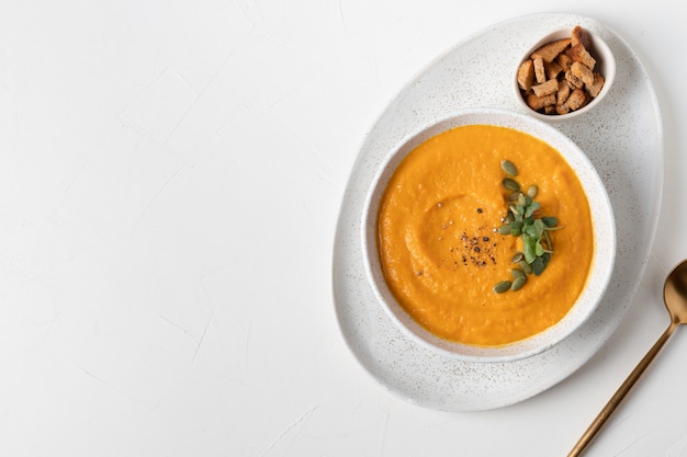 La sopa de calabaza sirve galletas y microgreens aislados en el cuadro blanco. Vista desde arriba.