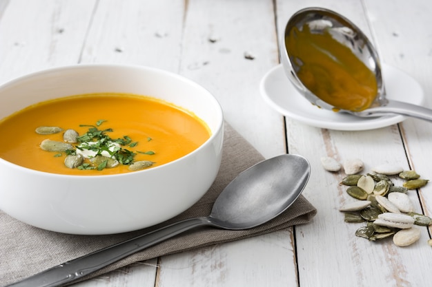 Sopa de calabaza en un tazón en madera rústica blanca