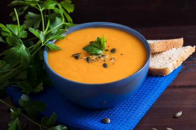 Sopa de calabaza en un tazón servido con perejil, aceite de oliva y semillas de calabaza.