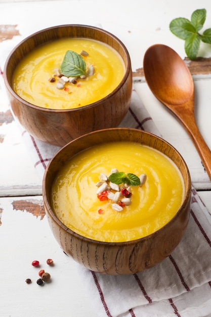 Sopa de calabaza triturada con especias en tazones de madera sobre tableros de luz.