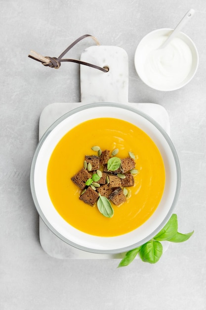 Sopa de calabaza y zanahoria asada de otoño de temporada con crutones de pan de centeno y crema sobre un fondo de hormigón ligero Vista superior