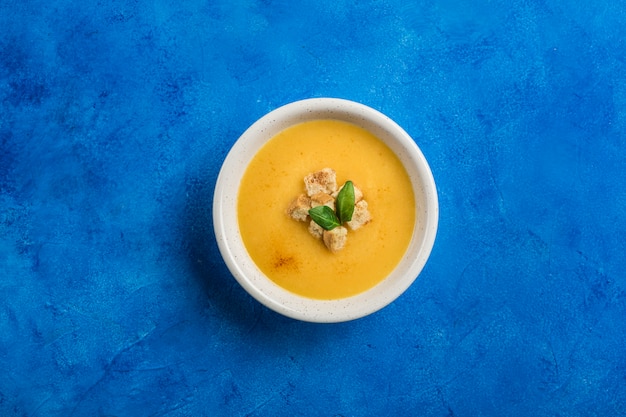 Sopa de calabaza y zanahoria con crema y espinacas con galletas sobre un fondo azul clásico.