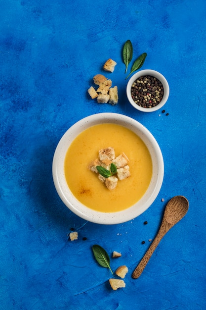 Sopa de calabaza y zanahoria con crema y espinacas con galletas sobre un fondo azul clásico.