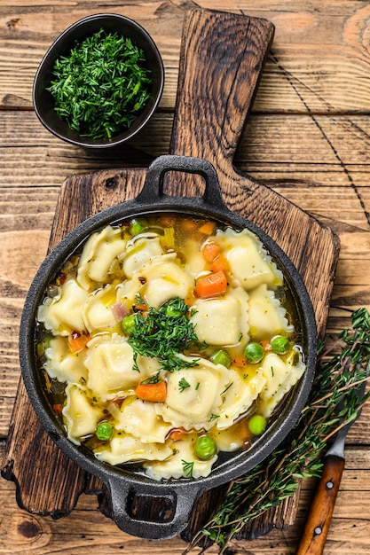 Sopa de caldo con pasta de ravioles albóndigas en una sartén. Fondo de madera. Vista superior.