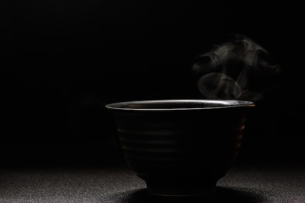 Sopa caliente en un tazón negro sobre mesa de madera, vapor de alimentos y espacio de copia, enfoque selectivo. Concepto de alimentos frescos