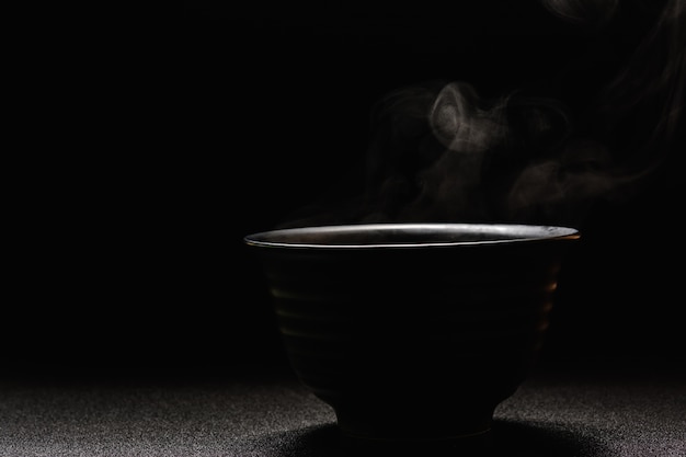 Sopa caliente en un tazón negro sobre mesa de madera, vapor de alimentos y espacio de copia, enfoque selectivo. Concepto de alimentos frescos