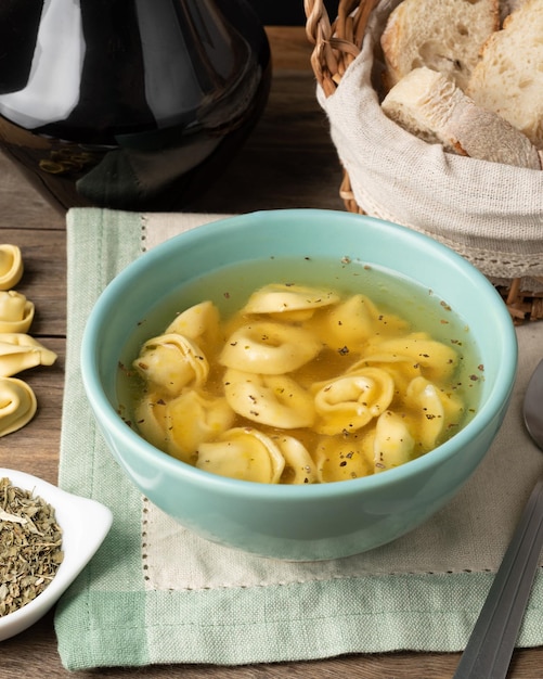 Sopa cappelletti o tortellini brodo en un bol con rebanadas de pan y condimentos sobre una mesa de madera